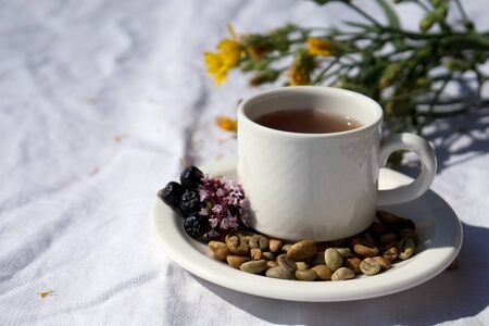 Coffee composition  with  white cup    of herbal coffe with herb , beans of coffe,  berry, mint, flower on  linen tableclothtable as backgroundの写真素材