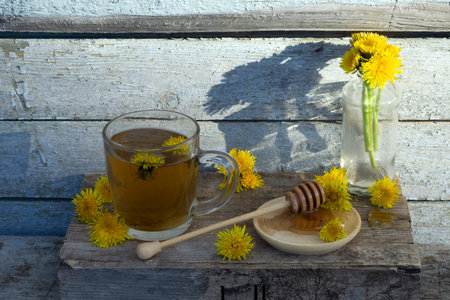Medicinal Tea from dandelion in glass cup with honey dandelion against a blue rustic wooden wall with copy spaceの写真素材
