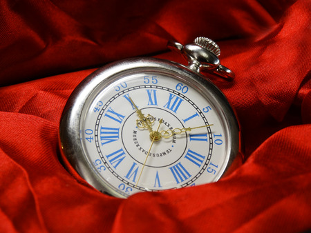 silver pocket watch on a background of red or scarlet cloth.のeditorial素材