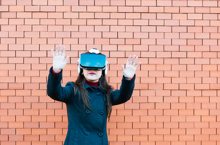 Handsome young woman using VR glasses with brickwall background and space for textの写真素材