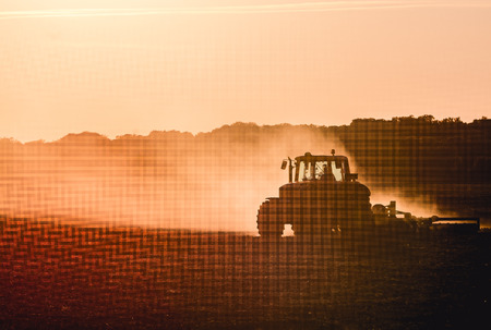 Silhouette of tractor working on a farm at twilight