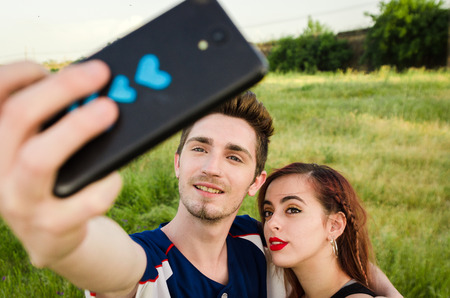 Happy couple in the field  taking a selfie with a smartphone. Smartphone with blue heartsの写真素材