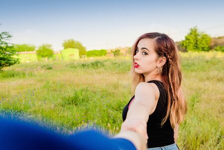 Beautiful young woman holding man's hand and leading him on fieldの写真素材