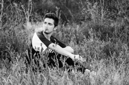 black and white portrait of lonely man smokong a cigarette in a fieldの写真素材