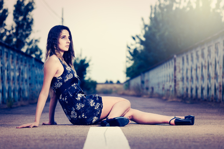 Dramatic portrait of a beautiful girl sitting in the middle of an empty roadの写真素材