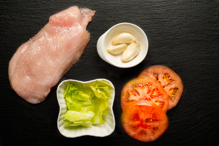 Raw chicken fillet with tomatoes, lettuce, garlic and salt . Food background, cooking ingredients. Fresh meat. Chicken breast.の写真素材