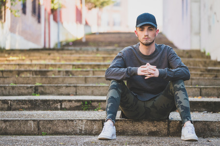 fashionable young man sitting on stairs in streetの写真素材
