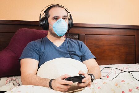 sick man with headphone and medical mask, playing videogames in the bedの写真素材