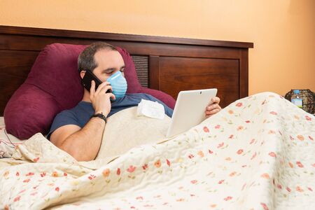 ill man using tablet and phone in the bed. Teleworkingの写真素材