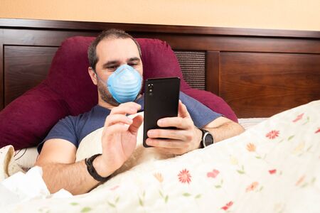 sick man laying in bed using smarthphoneの写真素材