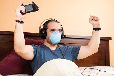 sick man with headphone and medical mask, playing videogames in the bedの写真素材