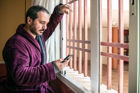 man looking through the window and using the smartphoneの写真素材
