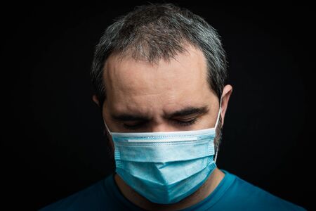 sad man with medical mask on black background. Man looking down