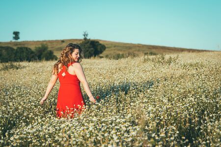 woman with red dress and poppy in hand in the field.の写真素材