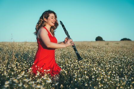 woman in a red dress playing the clarinet in a field of daisiesの写真素材