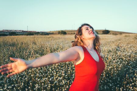 woman in red dress enjoying freedom in a field of daisiesの写真素材