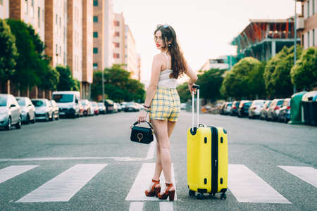 woman with a yellow suitcase and a bag on the street.の写真素材