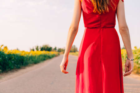 woman with red dress backwards in road with sunflowersの写真素材