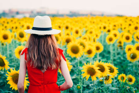 woman in red dress and hat entering sunflower field.の写真素材