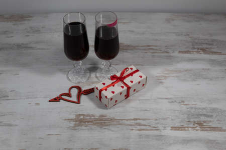 Two glasses of wine, one of which has a trace of lipstick. Near a box with a ribbon and a heart pierced by an arrow.の写真素材