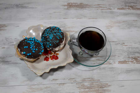 On the table on the openwork saucer are two delicious cakes decorated with chocolate icing. Next to the saucer is a cup of tea.の写真素材