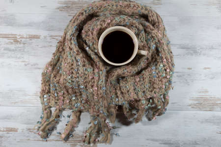 Top view. A cup of coffee is wrapped in a warm knitted winter scarf.の写真素材