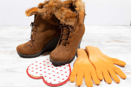 Two winter women's shoes, one of which with a toe stepped on a large heart, framed in red. Nearby are women's knitted winter gloves.の写真素材