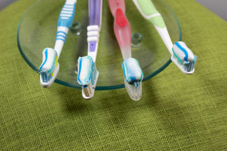 On a green background on a transparent saucer are four multi-colored toothbrushes with toothpaste.