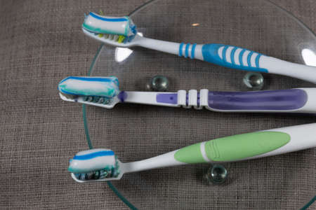 Closeup. On a transparent saucer, on a gray background are three multi-colored toothbrushes with...