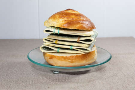 On a gray background on a transparent saucer lies a sandwich with bundles of money tied with...