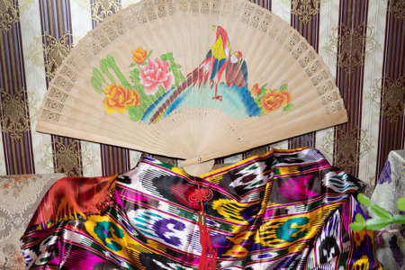 Against the background of the wall with dark wallpaper, there is an old large Chinese fan and Asian...