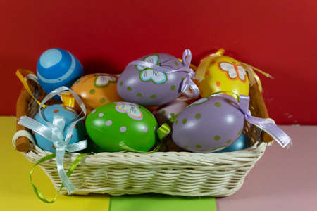 In a wicker basket on a red background lay multi-colored Easter eggs.の写真素材