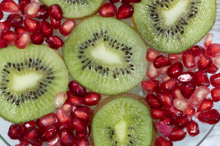 Close-up. On a transparent plate are pomegranate seeds and kiwi slices.の写真素材