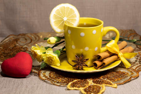 A cup of tea with lemon stands on the table. On a saucer are cinnamon sticks, star anise and yellow...