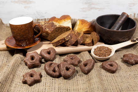 On jute fabric lies sliced rye bread, white wheat buns, cookies, a wooden spoon with seeds. Nearby...