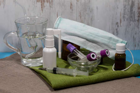 On napkins there is a throat spray, tea tree oil, a Mahold inhaler in a glass, a medical mask. In front are tubes and syringe.の写真素材
