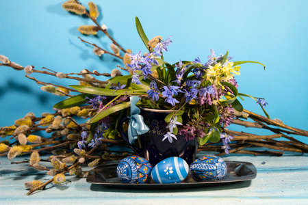 On a metal tray is a blue cup with spring forest flowers. Nearby are easter eggs. In the background...