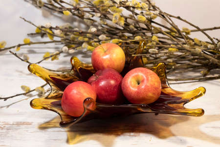 Ripe apples lie in a beautiful red vase. In the background there is a bouquet of willow branches.の写真素材