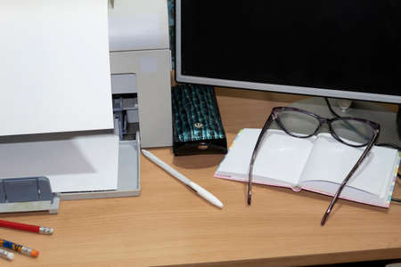 Workplace organized at home for remote work. On the table is a computer, printer, glasses, notebook,...