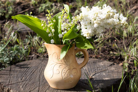 On an old stump in a clay pot is a white lilac and lilies of the valley.の写真素材
