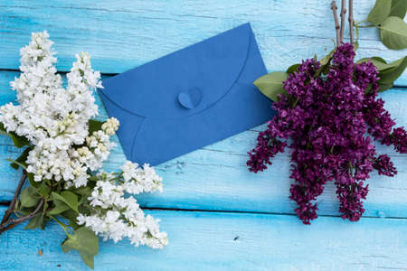 An envelope lies on a blue background. In the corners there are several branches of white and purple lilacs.の写真素材