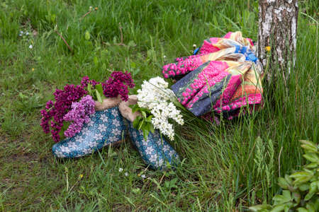 There are two womenâs spring boots in the grass. In one is a purple lilac, in the other is white. Nearby lies a folded bright female umbrella.の写真素材