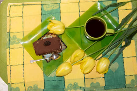 View from above. On the table is a cup of tea and a plate with a slice of cake and a spoon. Nearby are yellow tulips.の写真素材