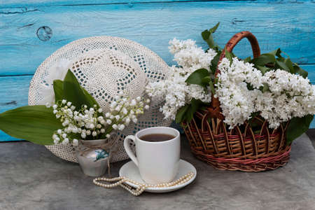 On the table is a basket with white lilac, a bouquet of lilies of the valley, a cup of tea. Nearby...