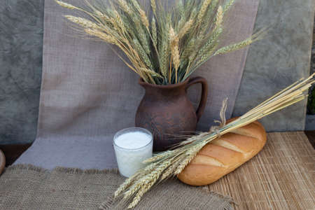 On the table is a glass of milk, lies white bread and ears of wheat. In the background is a jug with ears of wheat.の写真素材