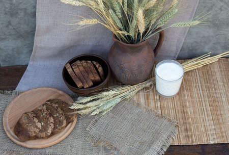 Ears of wheat, sliced black bread and a glass of milk are on the table.の写真素材