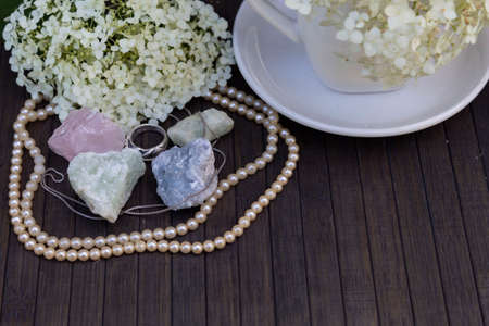 On a wooden background are natural semiprecious stones - rose quartz, aquamarine, prenite, celestine. Nearby there is a silver ring, chain and necklace. Behind there are hydrangea flowers.の写真素材