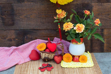 A Chinese lantern hangs over the table. There are yellow roses in a vase on the table. Nearby are calendula flowers, hearts and a key. A wicker car with scarlet hearts stands on the side.の写真素材