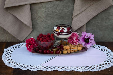 On a metal tray are yellow raspberries, ripe cherries and petunia flowers. There is a red raspberry...