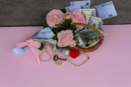 View from above. There is a basket with money on the table, a bouquet of pink roses wrapped in banknotes, a red heart, beads and a key.の写真素材
